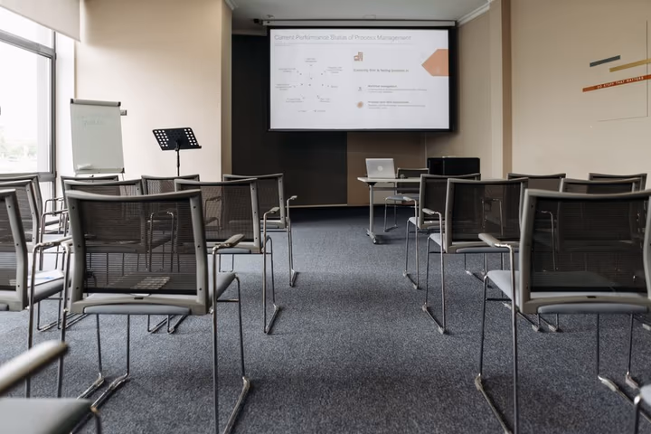 Une salle de conférence vide avec des chaises en rangées, un écran de projection et un pupitre de présentation prêt pour une formation.
